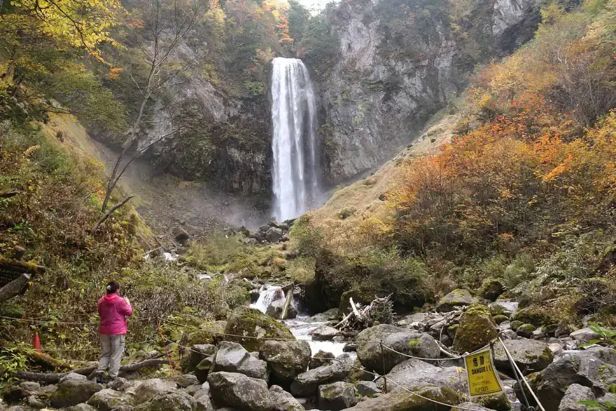Waterfall descending a rocky cliff surrounded by autumn foliage