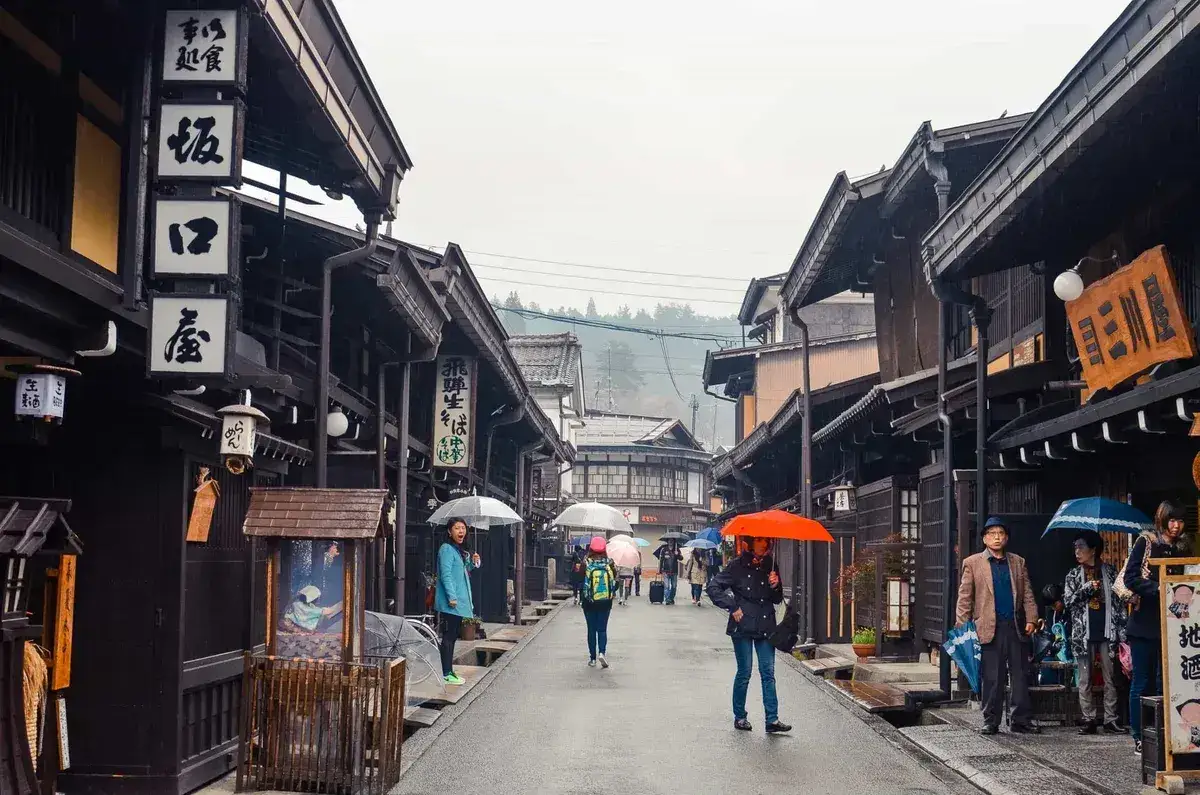 Visitors with umbrellas on a street lined with wooden shops